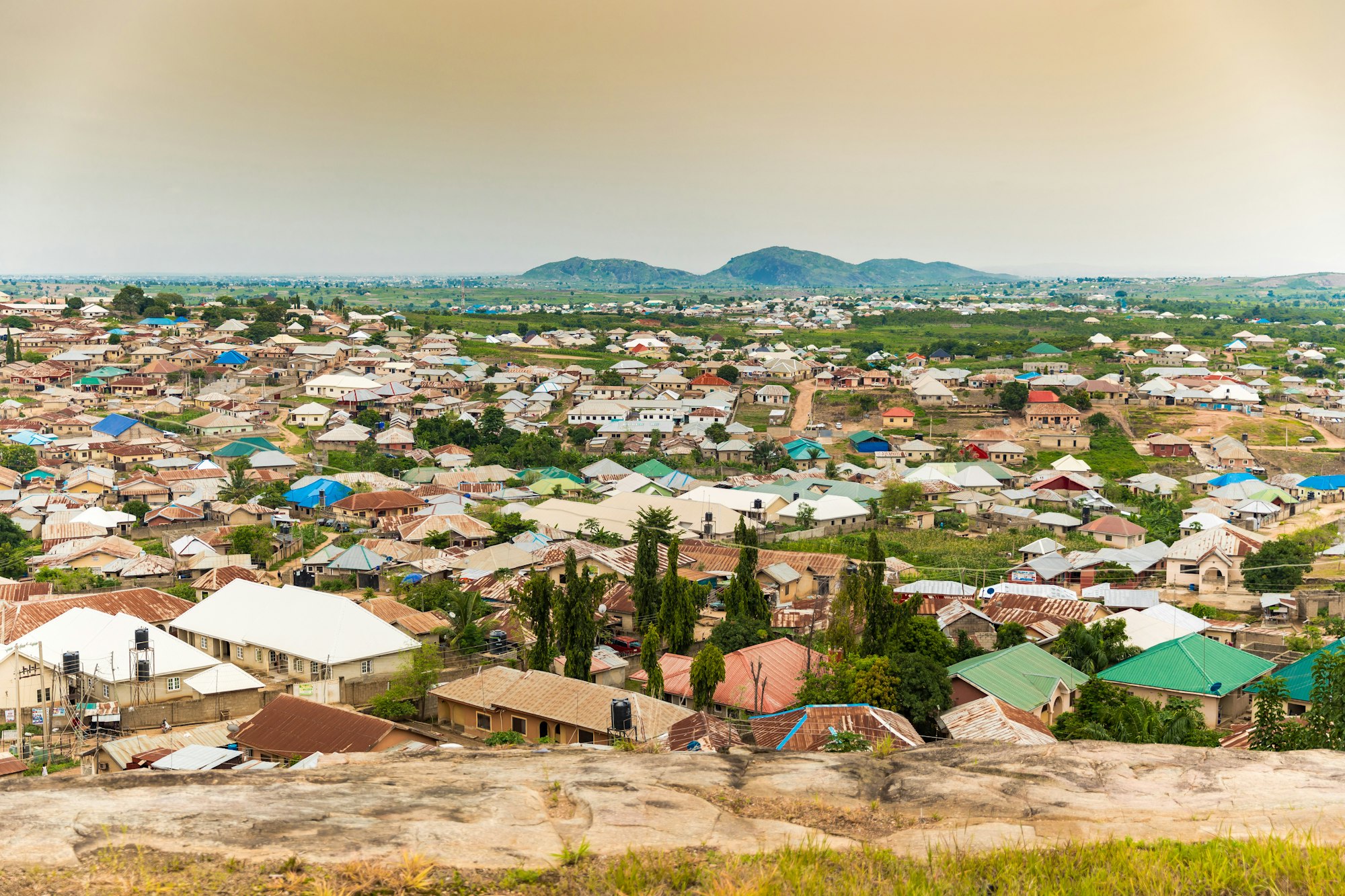 Rooftops of a growing Abuja settlement with hills on the horizon